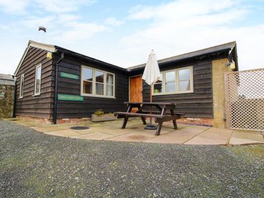 A cottage exterior with wooden walls a picnic table and umbrella on the patio at Norton Cottage in Craven Arms