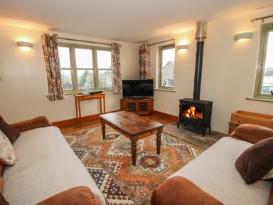 A living room with two sofas coffee table wood stove and television at Norton Cottage in Craven Arms