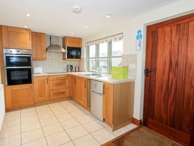 A kitchen with wooden cabinets oven microwave kettle and a bread bin next to a window and a wooden door at Norton Cottage in Craven Arms