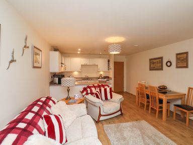 An open living room with white sofas red and white pillows and a kitchen with white cabinets at Cadliam in Whitby