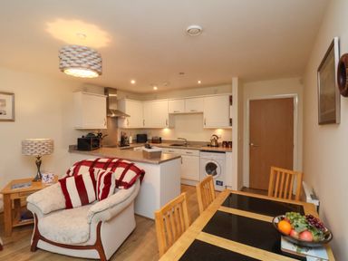 A kitchen and dining area with white cabinets a wooden dining table with fruit a cushioned armchair and a wooden door at Cadliam in Whitby