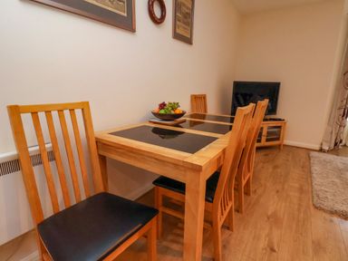 A dining area with a wooden table and chairs a bowl of fruit on the table a television on a wooden stand and framed pictures on the wall at Cadliam in Whitby