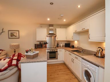 A kitchen with white cabinets a stove microwave washing machine and kettle at Cadliam in Whitby