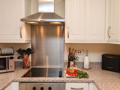 A kitchen with white cabinets a stainless steel stove and hood a microwave and utensils on the countertop at Cadliam Whitby