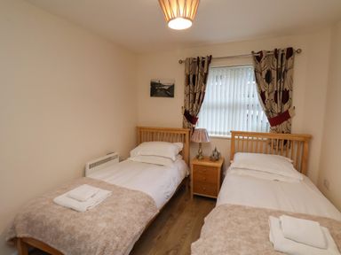A bedroom with two single beds a nightstand window with curtains and a lamp at Cadliam Whitby