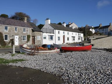 Three small boats on a pebbled shore in front of stone and white houses at Old Tollgate in Gwalchmai near Llangefni