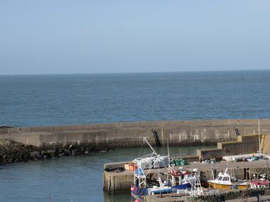 A harbor with fishing boats docked next to a concrete pier and the sea in the background at Old Tollgate Gwalchmai near Llangefni