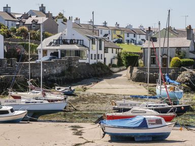 A coastal village scene with boats on a sandy shore and houses in the background at Old Tollgate in Gwalchmai near Llangefni