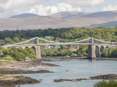 A large suspension bridge over a body of water with hills and trees in the background at Old Tollgate in Gwalchmai near Llangefni
