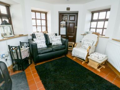 A sitting room with a black leather sofa and a wooden rocking chair with cushions at Old Tollgate in Gwalchmai near Llangefni