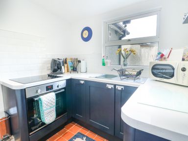 A kitchen with dark cabinets an oven microwave air fryer and a window with yellow flowers at Old Tollgate in Gwalchmai near Llangefni