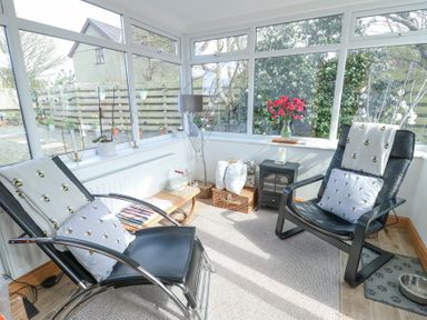 A sunroom with two black chairs with bee-patterned cushions a small table with magazines a lamp a basket with pillows and flowers on a windowsill at Old Tollgate in Gwalchmai near Llangefni