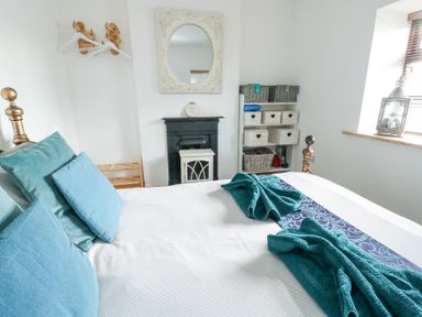 A bedroom with a bed with blue pillows and towels a mirror above a fireplace and shelves with baskets at Old Tollgate in Gwalchmai near Llangefni