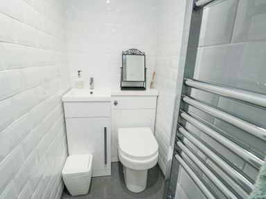 A small bathroom with a toilet a cabinet with a sink a mirror soap dispenser a small trash bin and a chrome towel radiator at Old Tollgate in Gwalchmai near Llangefni