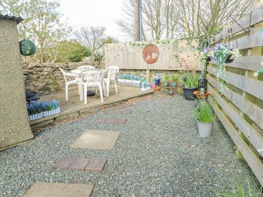 A small garden patio area with plastic chairs and table surrounded by potted plants and stone wall at Old Tollgate in Gwalchmai near Llangefni