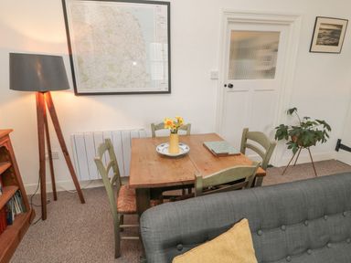 A dining area with a wooden table and four chairs a floor lamp a framed map on the wall a plant on a stand and a gray sofa in Lavender Cottage in Glanton