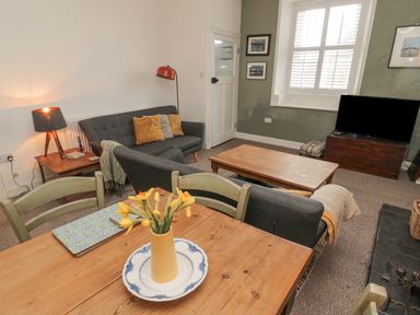 A living room with a wooden dining table and yellow flowers a sofa a coffee table a television and a window at Lavender Cottage in Glanton