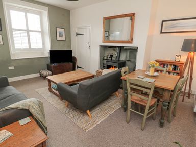 A living room with a fireplace a wooden dining table with chairs and a television at Lavender Cottage in Glanton