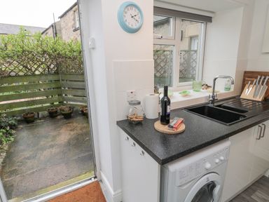 A kitchen counter with a sink a washing machine and various items next to an open door leading to a small outdoor area with potted plants at Lavender Cottage in Glanton