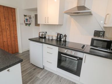 A kitchen with white cabinets black countertops an oven microwave toaster kettle and refrigerator at Lavender Cottage in Glanton