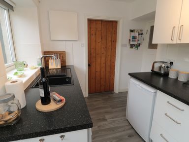 A kitchen with black countertops a wooden door a sink a bottle a toaster and cabinets at Lavender Cottage in Glanton