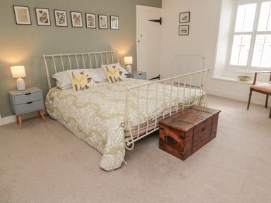 A bedroom with a metal bed frame bedding bedside tables lamps a wooden chest and framed pictures on the wall at Lavender Cottage in Glanton