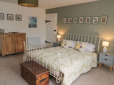 A bedroom with a bed with floral bedding two bedside tables with lamps a wooden chest at the foot of the bed a wooden cabinet and framed pictures on the walls at Lavender Cottage in Glanton