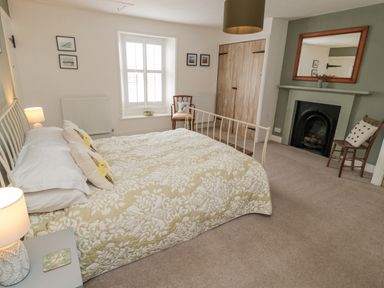 A bedroom with a double bed a fireplace two chairs and built in wooden cupboards at Lavender Cottage in Glanton
