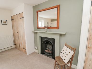 A room with a fireplace containing pinecones a chair with a cushion a wooden closet and a wall mirror at Lavender Cottage in Glanton