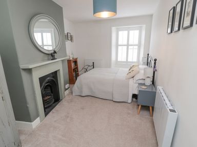 A bedroom with a bed a bedside table a fireplace a round mirror and a window at Lavender Cottage in Glanton