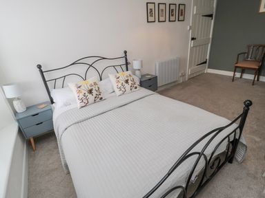 A bedroom with a double bed with floral pillows bedside tables with lamps a door and a wooden chair at Lavender Cottage in Glanton