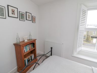 A bedroom corner with a wooden bookshelf, framed pictures on the wall, and a window with shutters at Lavender Cottage in Glanton