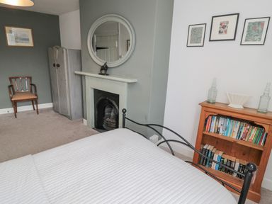 A bedroom with a bed white bedding a fireplace a wooden chair a wooden bookcase with books and decor at Lavender Cottage in Glanton