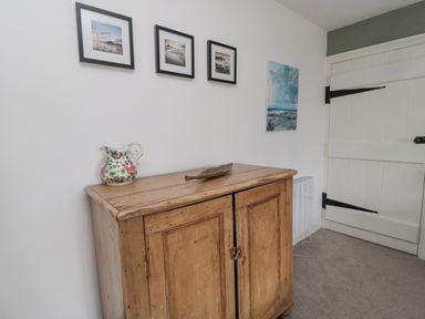 A wooden cabinet with a floral pitcher and decorative item on top below framed pictures and a painting near a white door at Lavender Cottage in Glanton