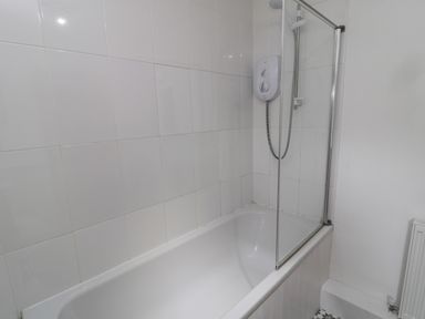 A bathroom with a white bathtub shower unit and a glass shower screen at Lavender Cottage in Glanton