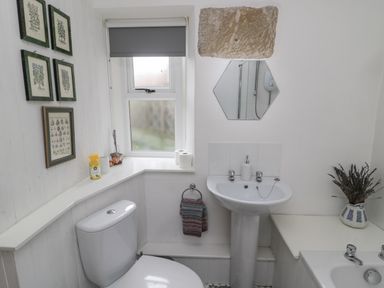 A bathroom with a toilet sink bathtub hexagon mirror and framed pictures on the wall at Lavender Cottage in Glanton