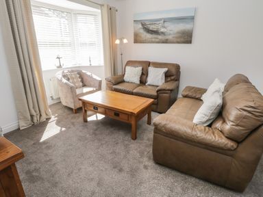 A living room with two brown leather sofas a wooden coffee table an upholstered armchair and a window with blinds and curtains at Seadrift The Bay near Filey