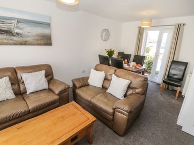 A living room with brown leather sofas and a wooden coffee table and a dining table set with black chairs and flowers at Seadrift The Bay near Filey