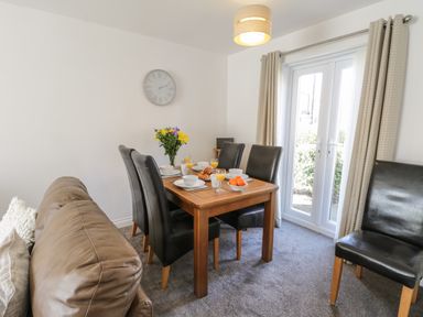 A dining area with a wooden table set for breakfast with black chairs and beige curtains at Seadrift The Bay near Filey