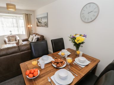 A dining table set with plates bowls croissants and orange juice next to a living room with sofas and a chair at Seadrift The Bay near Filey