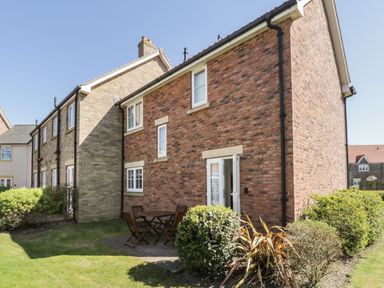 A brick house with white windows and a small patio table with chairs in a garden at Seadrift in The Bay near Filey