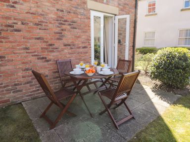 An outdoor patio with a wooden table and four wooden chairs set with plates cups and glasses near a brick wall at Seadrift The Bay near Filey