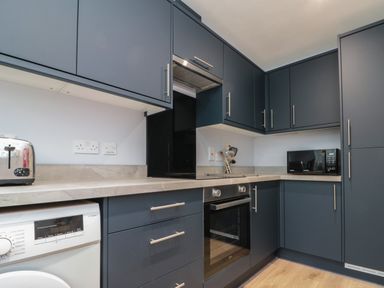 A kitchen with dark cabinets a built-in oven a microwave toaster and a washing machine at Seadrift The Bay near Filey