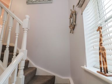 A staircase with white railing and grey carpet with a wooden giraffe on a windowsill at Seadrift in The Bay near Filey
