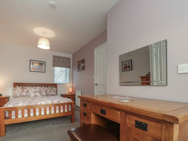 A bedroom with a wooden bed and matching furniture including a desk and bedside tables at Seadrift The Bay near Filey