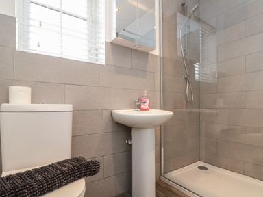 A bathroom with a toilet a pedestal sink with soap a shower area and a black towel on the toilet at Seadrift The Bay near Filey