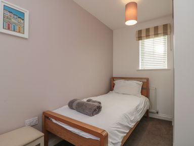 A small bedroom with a single wooden bed a rolled towel on the bed a window with blinds and a light fixture at Seadrift The Bay near Filey