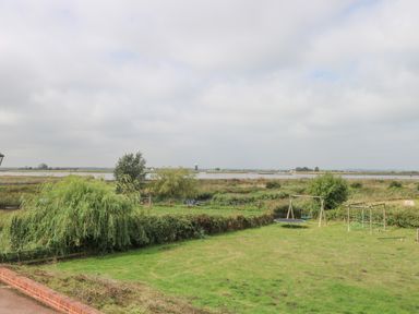 A grassy garden with wooden play equipment and a trampoline near a wetland and water body at Waveney View Cottage in Burgh Castle