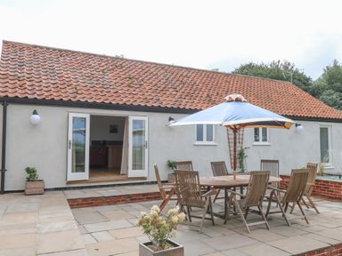 An outdoor patio area with a wooden table and chairs under a blue umbrella at Waveney View Cottage in Burgh Castle