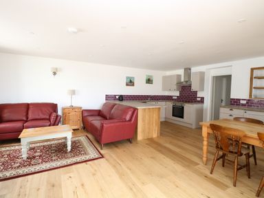 An open living area with two red sofas a wooden coffee table and rug near a kitchen with wooden dining table Waveney View Cottage in Burgh Castle